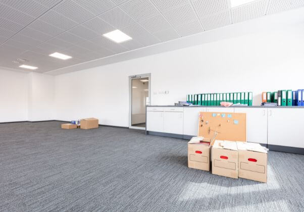 En tom kontorslokal med några kartonger på golvet, en whiteboardtavla och skåp längs väggen.